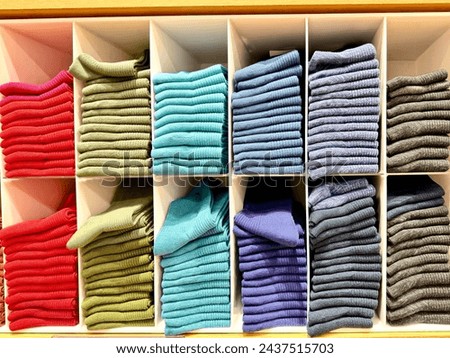 The arrangements of colors in clothes, home or shop to look attractive and tidy. Knitted clothes on shelf in a store. Neat row of clothes in assortment. Royalty-Free Stock Photo #2437515703