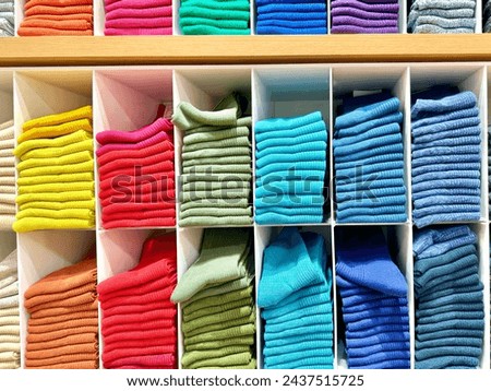 The arrangements of colors in clothes, home or shop to look attractive and tidy. Knitted clothes on shelf in a store. Neat row of clothes in assortment. Royalty-Free Stock Photo #2437515725