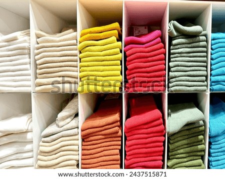 The arrangements of colors in clothes, home or shop to look attractive and tidy. Knitted clothes on shelf in a store. Neat row of clothes in assortment. Royalty-Free Stock Photo #2437515871
