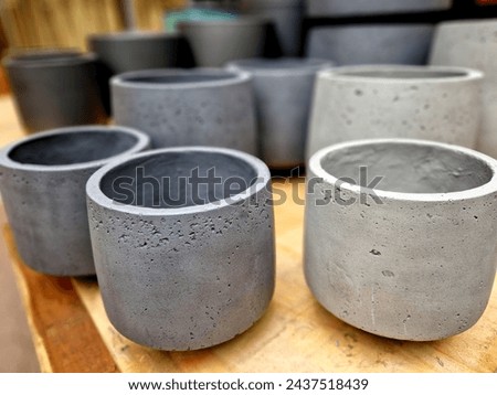 gray concrete flower pots, lined up in a warehouse in rows for sale. plastic white tubs of bricks stacked on top of each other. production of cheap design containers for plant, table