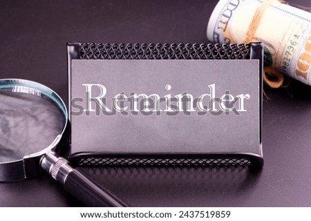 reminder word on the business card next to a roll of money and a magnifying glass on a black background