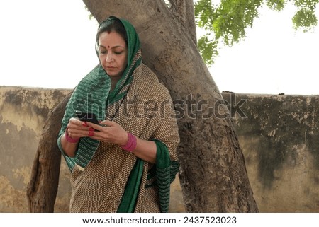 Portrait of mature middle class rural working woman using smartphone at home to make online payment , shopping on internet with cellphone secure banking service system concept in village. Royalty-Free Stock Photo #2437523023