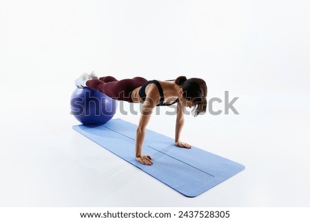 Sportive young woman with fit body training, standing in plank position on fitness ball isolated over white studio background. Concept of sport, health and body care, fitness app, exercises templates