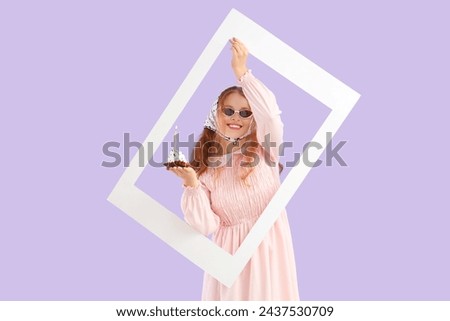 Beautiful young happy woman with birthday cupcake and frame on purple background