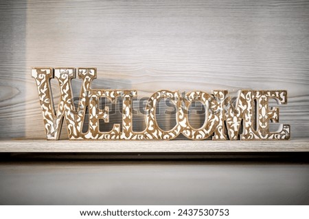 Close-Up of Vintage 'Welcome' Wooden Sign on Light Wood Background. Rustic, weathered lettering adds charm and character to this welcoming sign, perfect for home decor projects, hospitality themes.