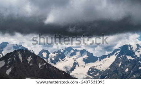 A dramatic scene, dark, heavy clouds loom over a mountain range, signaling approach of a storm. A pre-thunderstorm sky indicates that a cold snap and precipitation, rain, snow or hail, is imminent Royalty-Free Stock Photo #2437531395