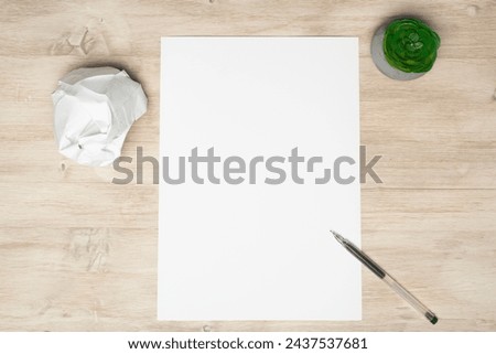 Top view, on a blank sheet of paper lying on a wooden table next to a crumpled sheet. A pen with a sheet of crumpled paper. Royalty-Free Stock Photo #2437537681