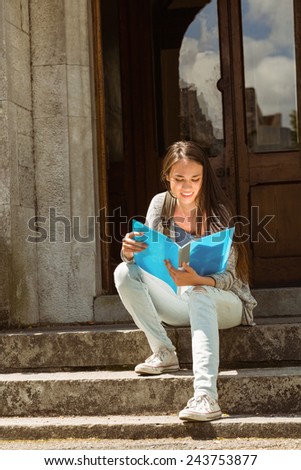 Smiling student sitting and reading book on steps at school