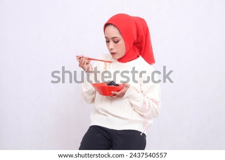 Asian woman wearing a hijab candidly looking down at noodles using chopsticks and a bowl containing ramen (Chinese food). Beautiful Muslim women use culinary, food and health content