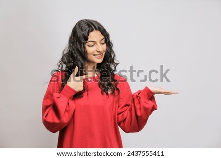 Happy Pakistani girl showing product. Beautiful Pakistani girl with curly hair pointing to side .Presenting your product. Isolated on white background. Expressive facial expressions Royalty-Free Stock Photo #2437555411