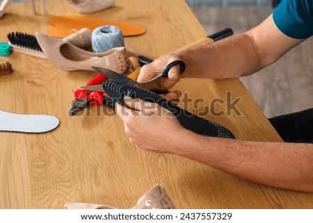Mature shoemaker cutting insole at table in workshop, closeup