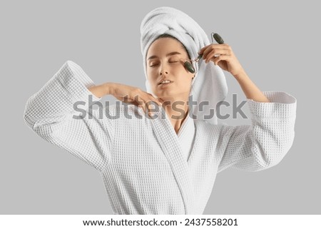 Young woman with towel massaging her face after shower on light background