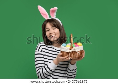 Easter celebration. Happy woman with bunny ears and wicker basket full of painted eggs on green background