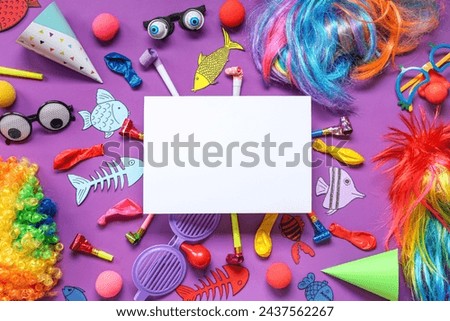 Blank card with paper fishes and party decor on purple background. April Fools Day celebration Royalty-Free Stock Photo #2437562267