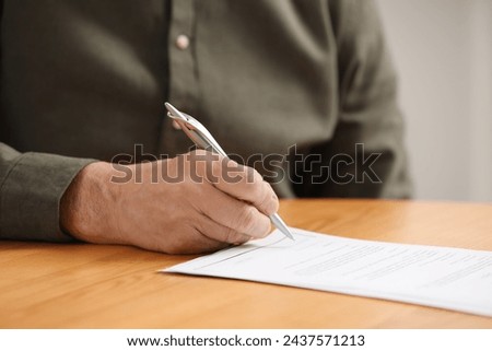 Senior man signing Last Will and Testament at wooden table indoors, closeup