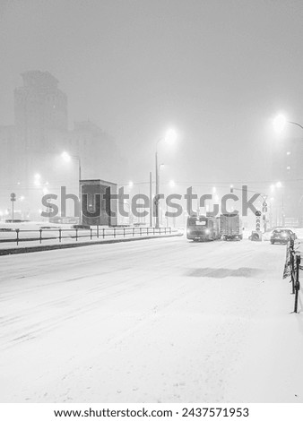 View of a city street in the evening during heavy snowfall. Public transport and cars in the light of street illumination during a snowstorm. Black and white photo.