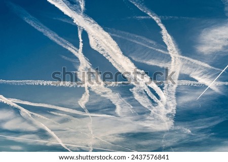 Tangle of partially dissolving and crossing contrails in the blue sky with light clouds and cirrus clouds
