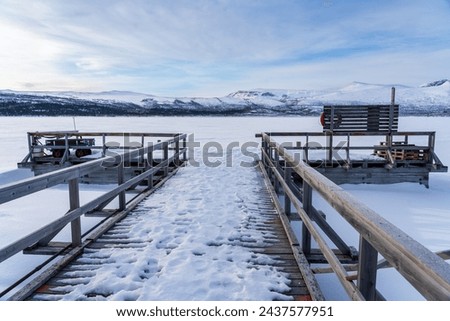 Winter landscape with wooden boat dock covered in snow in front of an icy snow-covered lake in Swedish Lapland Royalty-Free Stock Photo #2437577951