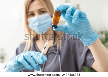 Biological hazard. Epidemic of the Chinese coronavirus. An woman in a protective mask holds an injection syringe and vaccine. Vaccine flu, coronavirus, ebola, TB. Royalty-Free Stock Photo #2437586335