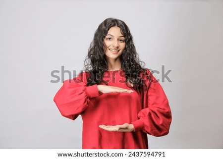 Young Pakistani woman holding something or nothing presenting a copy space as if holding a product, Wearing red sweatshirt, isolated over white background, Ad concept