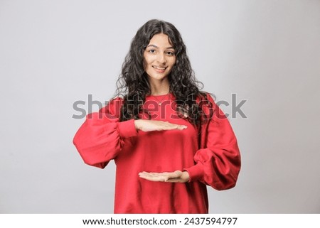 Young Pakistani woman holding something or nothing presenting a copy space as if holding a product, Wearing red sweatshirt, isolated over white background, Ad concept