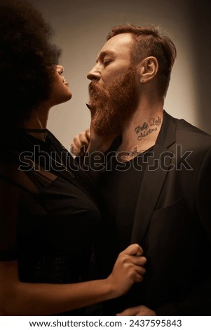 curly african american woman in black dress seducing tattooed boyfriend with beard, date night Royalty-Free Stock Photo #2437595843