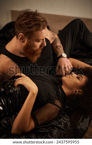 bearded man with tattoos seducing girlfriend in bedroom, passionate moment of multicultural couple Royalty-Free Stock Photo #2437595955