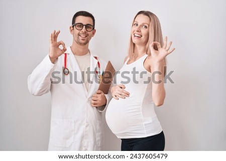 Young woman expecting a baby with doctor doing ok sign with fingers, smiling friendly gesturing excellent symbol 