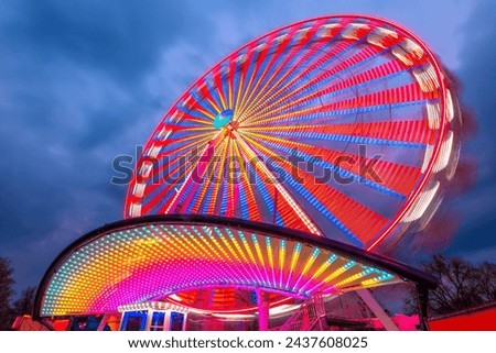 Colorful Ferris wheel at a funfair in Germany with motion blur. Glowing red, yellow lines and circles from long exposure light trails. Popular twilight ride at blue hour. Roundabout or merry-go-round. Royalty-Free Stock Photo #2437608025