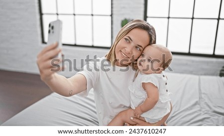 Happy mother and daughter taking confident selfie and capturing precious moments of love and togetherness in the comfy room sitting on bed, making picture with smartphone indoors, casual lifestyle.