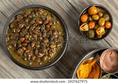 Black soybeans cooked in spices. Bhat ki Chudkani - a traditional dish of the Kumaon region. Pickled chilies and a box with spices on the side. Royalty-Free Stock Photo #2437627971