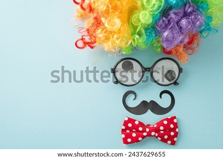 April Foolery display: top view photo with humorous goggles, buffoon's wig, neckwear, and pretend mustache, assembled to imitate a person's facial features on a pastel blue canvas, space for messaging Royalty-Free Stock Photo #2437629655