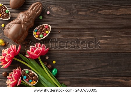 Charming Easter sweet treats concept. Overhead photo of chocolate eggs broken open with colorful candies spilling out, chocolate bunny, fresh tulips placed on wooden background, with space for text