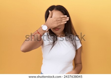 Young arab woman wearing casual white t shirt over yellow background covering eyes with hand, looking serious and sad. sightless, hiding and rejection concept  Royalty-Free Stock Photo #2437638045