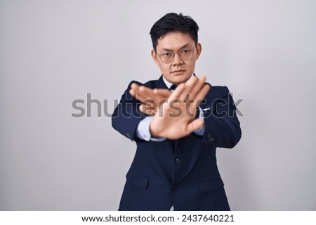 Young asian man wearing business suit and tie rejection expression crossing arms and palms doing negative sign, angry face 