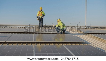 Solar panel technicians Workers in reflective gear are discussing over a laptop on a vast solar array during a bright day sunset sky in the background