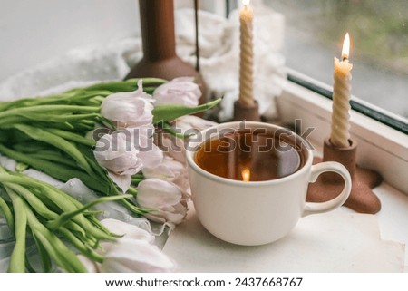 Cup of tea, bouquet of pink tulips and candles, spring aesthetics.