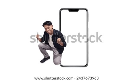 Full body of young very happy and excited handsome asian man he is wearing black shirt near large blank screen mobile phone workspace mockup area doing winning gesture isolated on white background