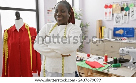 Confident black woman with braids standing arms crossed in tailor shop among sewing materials