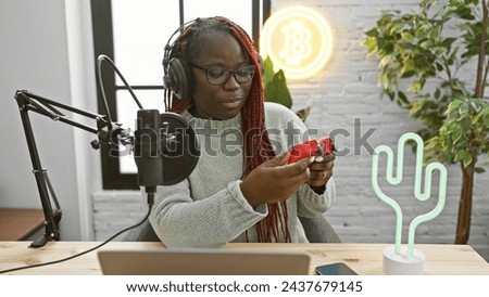 African american woman with braids examines a joystick in a modern radio studio interior.