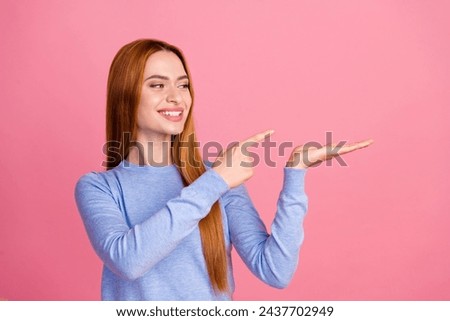 Portrait of satisfied girl with foxy hair wear blue pullover look directing at offer on palm empty space isolated on pink color background Royalty-Free Stock Photo #2437702949
