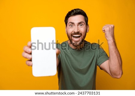 Photo portrait of attractive young man hold gadget white screen raise fists wear trendy khaki clothes isolated on yellow color background