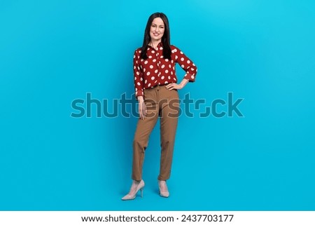 Full length photo of pleasant confident woman dressed dotted shirt brown pants keep arm on waist isolated on blue color background
