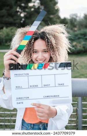 Young man with curly hair smiling after an outdoor cinema clapperboard. Concept: lifestyle, fun