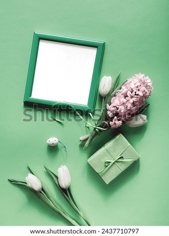 A picture frame with copy-space is placed next to a gift box and spring flowers, featuring white tulips and pink hyacinth in full bloom.