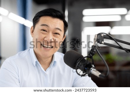 Close-up portrait of a young Asian man sitting in the office in front of a microphone and smiling at the camera.