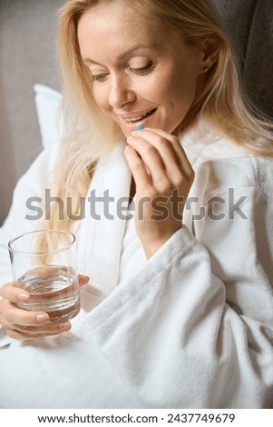 Smiling woman is taking medicine in her bedchamber Royalty-Free Stock Photo #2437749679