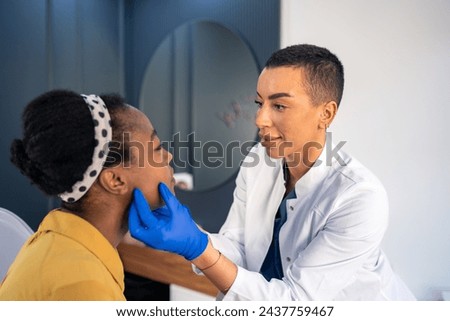 Young woman with dark skin tone at dermatology check up in beauty salon. Female dermatologist preparing female patient for beauty procedure. Royalty-Free Stock Photo #2437759467