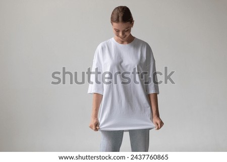 Beautiful blonde girl in a white oversized T-shirt and blue jeans posing on a gray background