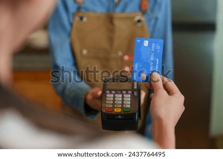 Beautiful young Asian business barista in dark blue shirt wearing brown apron holds credit card machine. Have female customer use credit card to swipe pay for the bakery coffee. Small family business